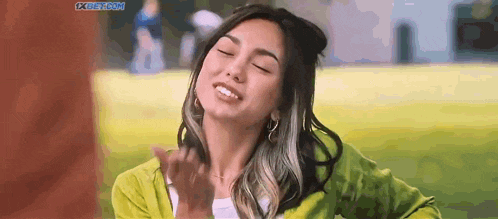 a woman in a green sweater is making a funny face while standing in the grass .