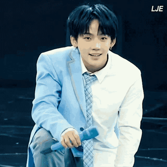 a young man in a suit and tie is holding a microphone and smiling