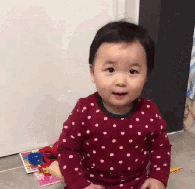 a baby is sitting on the floor wearing a red polka dot shirt and smiling .