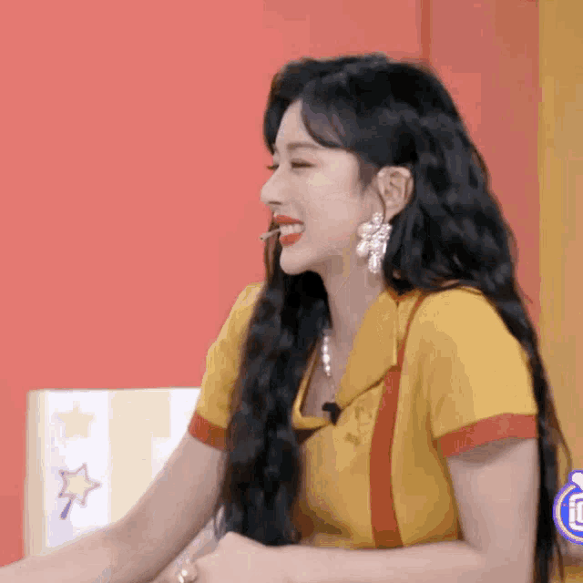 a woman with long black hair is wearing a yellow top and earrings