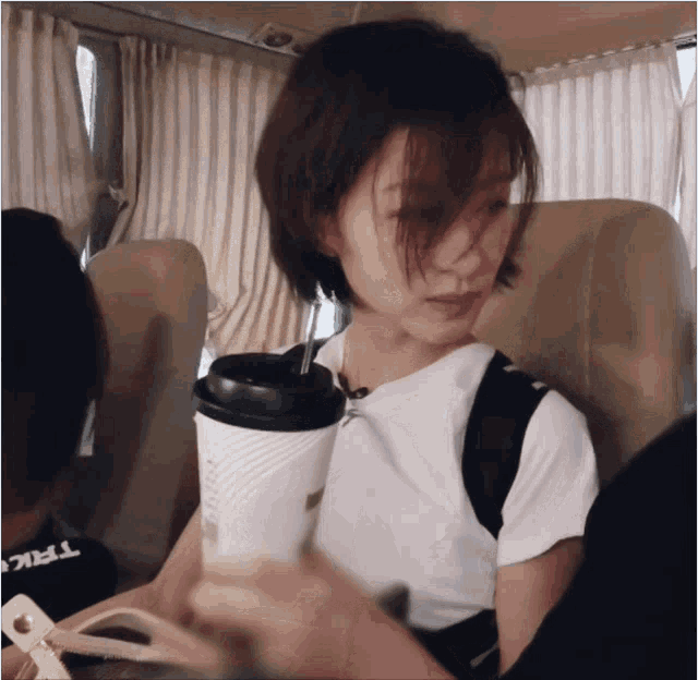 a woman sitting in a car with a cup of coffee and a trick shirt on