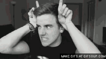 a black and white photo of a man making a devil horns sign with his hands .