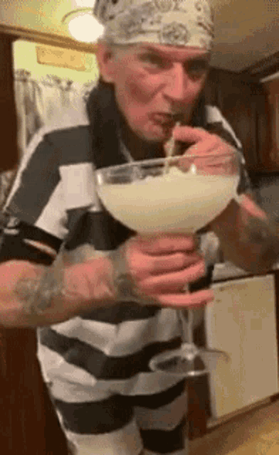 a man in a striped shirt is drinking from a large martini glass .