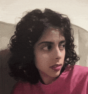 a woman with curly hair wearing a pink shirt looks to the side