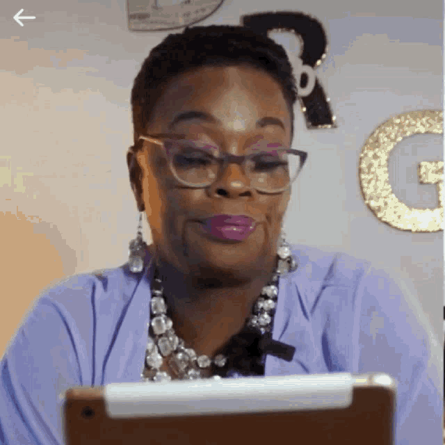 a woman wearing glasses and a purple shirt looks at a tablet