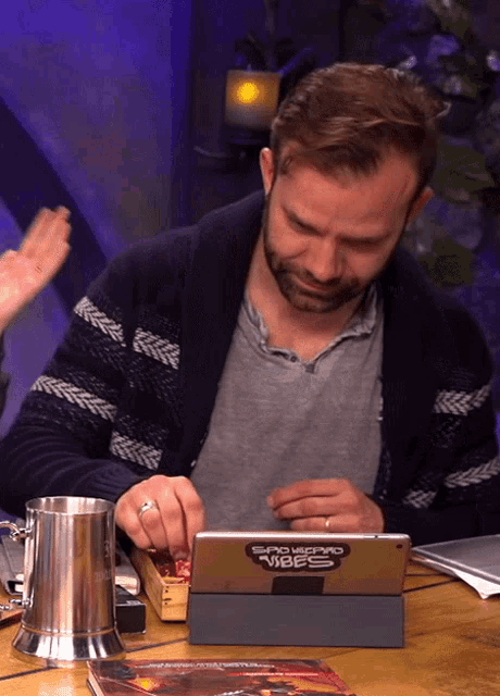 a man sits at a table playing a game on a tablet that says sand leopard video