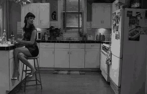 a woman is sitting on a stool in a kitchen with a bottle of wine .