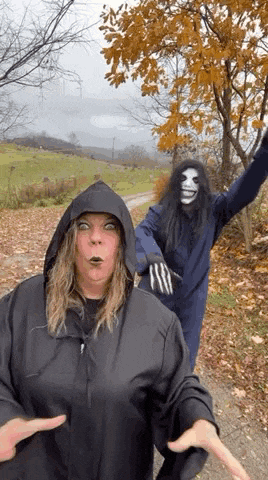 a woman in a hooded jacket is standing next to a man in a mask on a dirt road .
