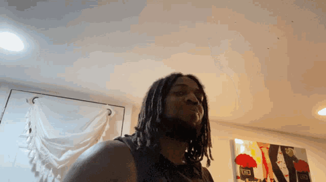 a man with dreadlocks stands in front of a painting of a woman
