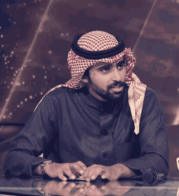 a man wearing a head scarf is sitting at a table with a microphone