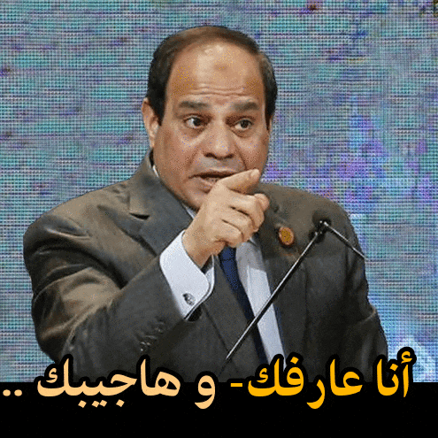 a man in a suit and tie speaking into a microphone with arabic writing below him