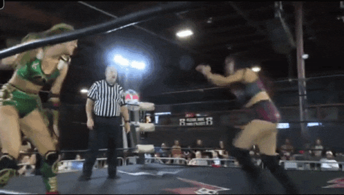 two women are wrestling in a ring with a referee and a scoreboard with the number 16 on it