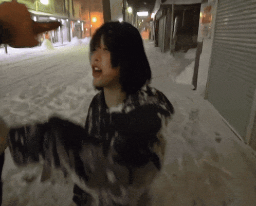a woman is covered in snow while a man throws a snowball at her