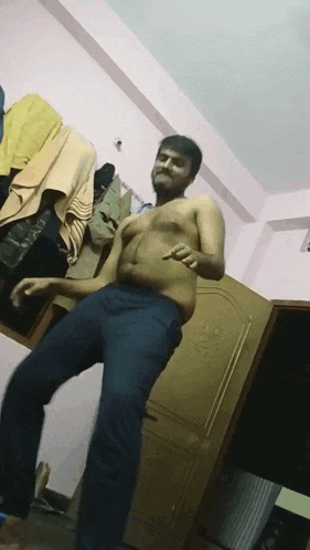 a shirtless man dancing in a room with clothes hanging on the wall