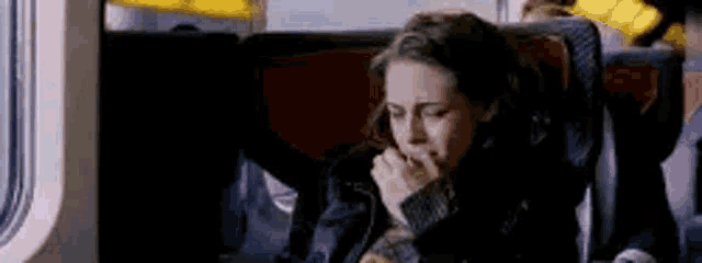 a woman is sitting on a train with her hand to her mouth .