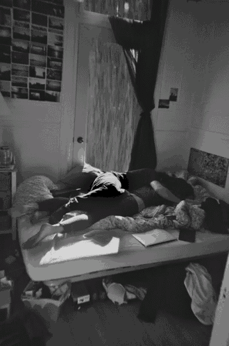a black and white photo of two people laying on a bed with pictures on the wall behind them