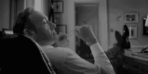 a man in a suit and tie is laying in a chair with his feet up and smoking a cigarette .
