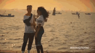 a man and a woman standing next to each other in front of the ocean