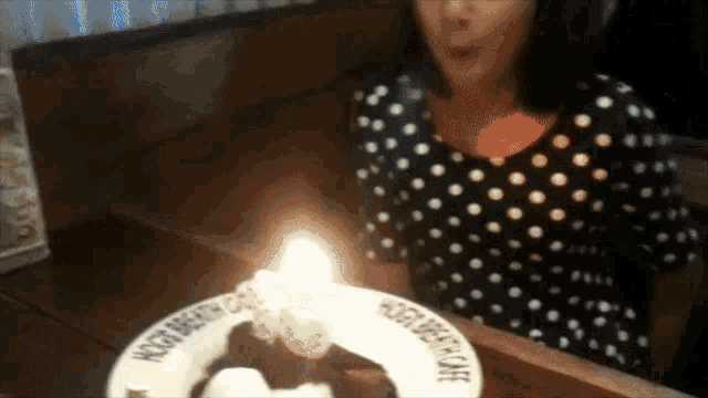 a woman blows out a birthday candle on a plate that says happy birthday on it