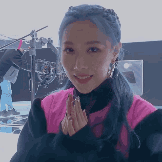 a woman with blue hair wearing a pink jacket and black turtleneck