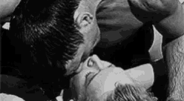 a black and white photo of a man kissing a woman on the forehead .
