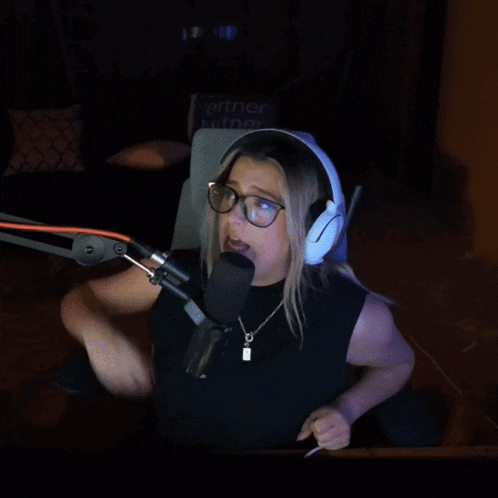 a woman wearing headphones and glasses is sitting in front of a microphone with the word hugs behind her