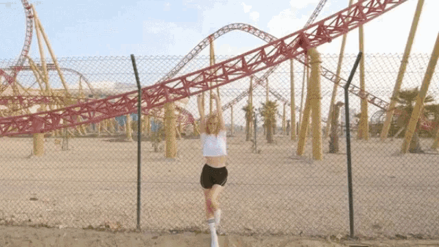 a woman is standing in front of a roller coaster