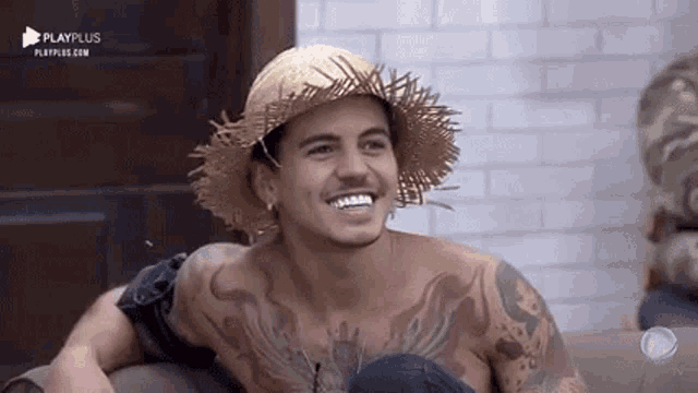 a shirtless man wearing a straw hat and a tattoo on his chest is smiling .