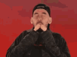 a man with a beard is laughing and holding his hands up in the air in front of a red background .