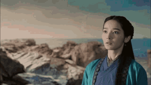 a woman in a blue kimono is standing in front of a rocky shoreline