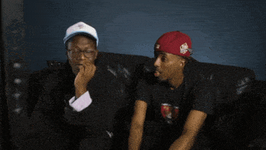 two men sitting on a couch one wearing a black shirt that says ' american psycho ' on it