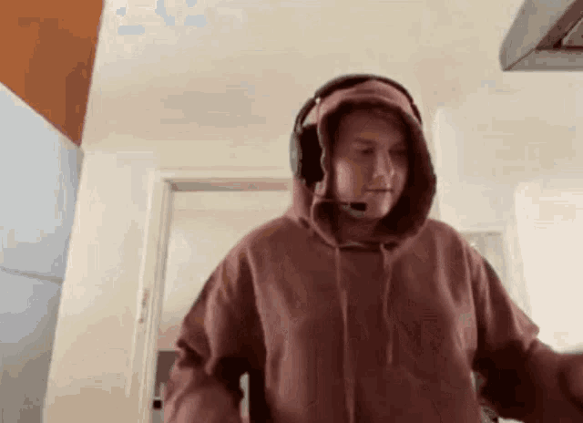 a man wearing headphones and a hoodie is standing in a room .