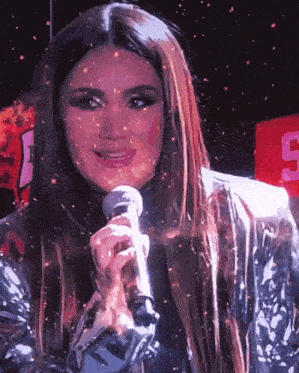 a woman singing into a microphone in front of a sign that says s