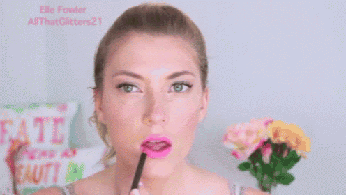 a woman is applying pink lipstick with a brush