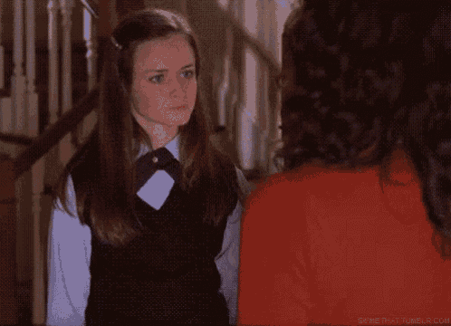 a girl in a school uniform is standing next to a woman in a red sweater .