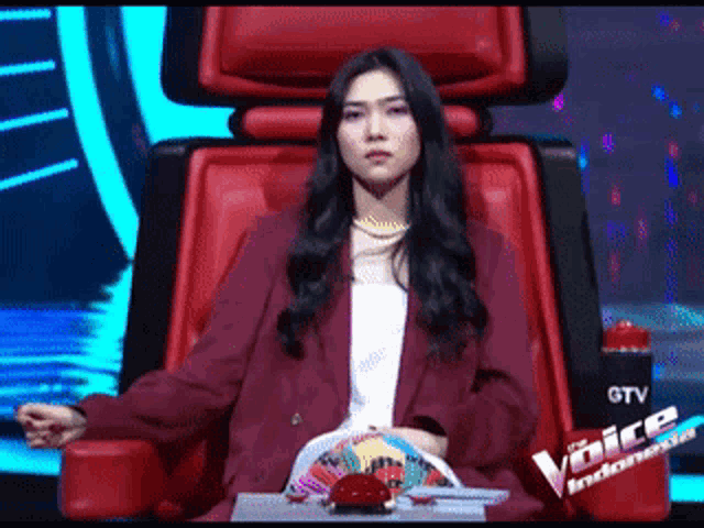 a woman in a red jacket is sitting in a red chair with the word voices indonesia written on it