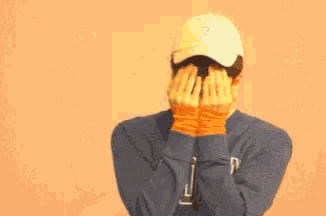 a man wearing a hat and a sweatshirt with the letter j on it is covering his face with his hands