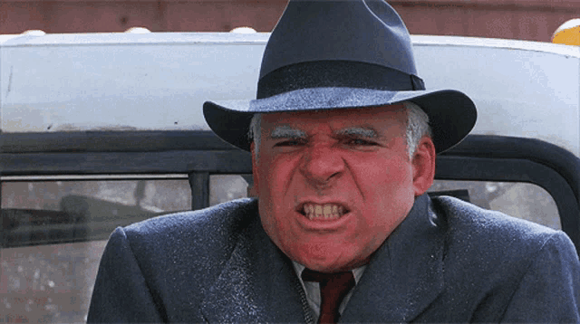 a man wearing a hat and a suit makes a funny face