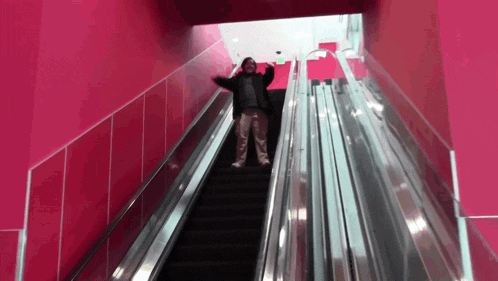 a man is standing on an escalator with a pink wall behind him