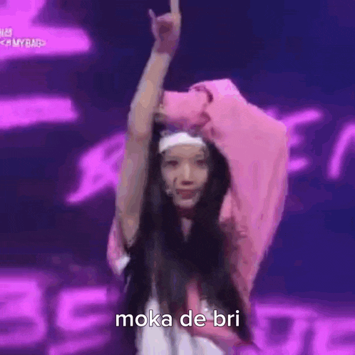 a woman in a pink jacket and headband is dancing on a stage in front of a purple background .