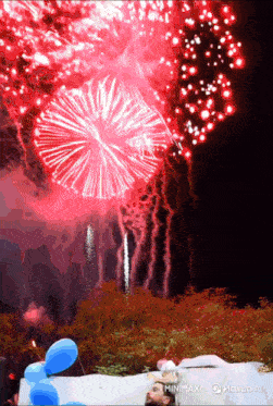fireworks are displayed in the night sky above a man in a bathtub with balloons