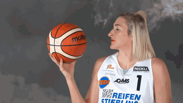 a female basketball player holds a molten basketball in her hand