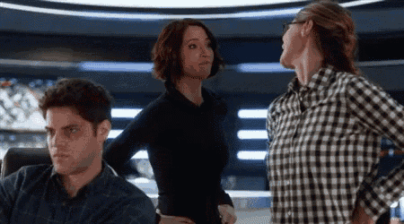 a man and two women are standing next to each other in a room . one of the women is wearing glasses .