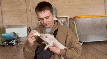a man is feeding a pig from a bottle while holding it