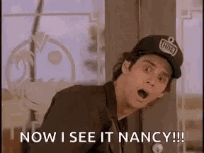 a man wearing a baseball cap is standing in front of a window and says `` now i see it nancy '' .