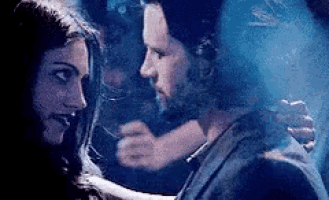 a man and a woman are standing next to each other in a dark room and looking at each other .