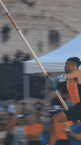 a man is jumping a pole in front of a crowd of people