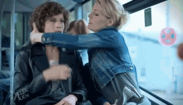 two women are sitting on a bus and one of them is holding another woman 's hair .