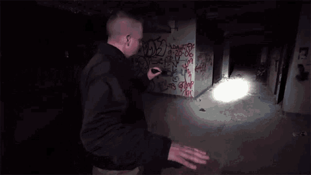 a man holding a flashlight in a dark room with graffiti on the walls including the letters d2