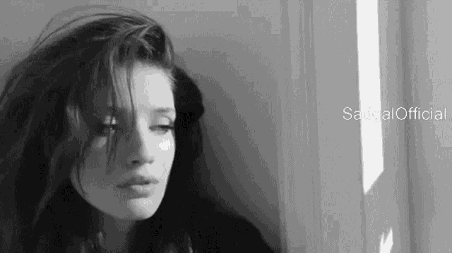 a black and white photo of a woman leaning against a wall looking out a window .